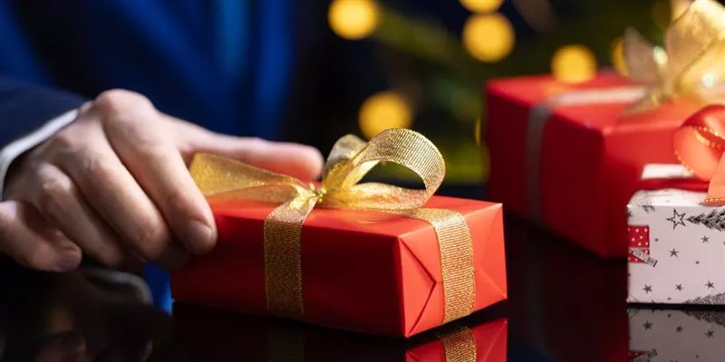 hombre sostiene un regalo de navidad en la mano con envoltorio rojo y moño dorado 