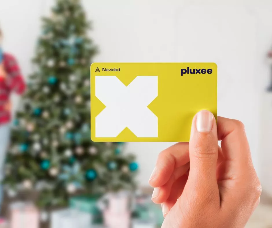 Mujer sosteniendo en su mano una tarjeta Pluxee Navidad con decoración navideña de fondo 