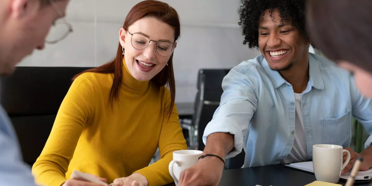 Cuatro personas en la oficina trabajando en conjunto mientras ríen y comparten un café 