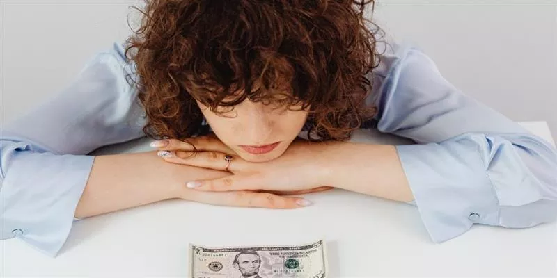 Colaboradora preocupada por su situación financiera, con un billete sobre el escritorio 