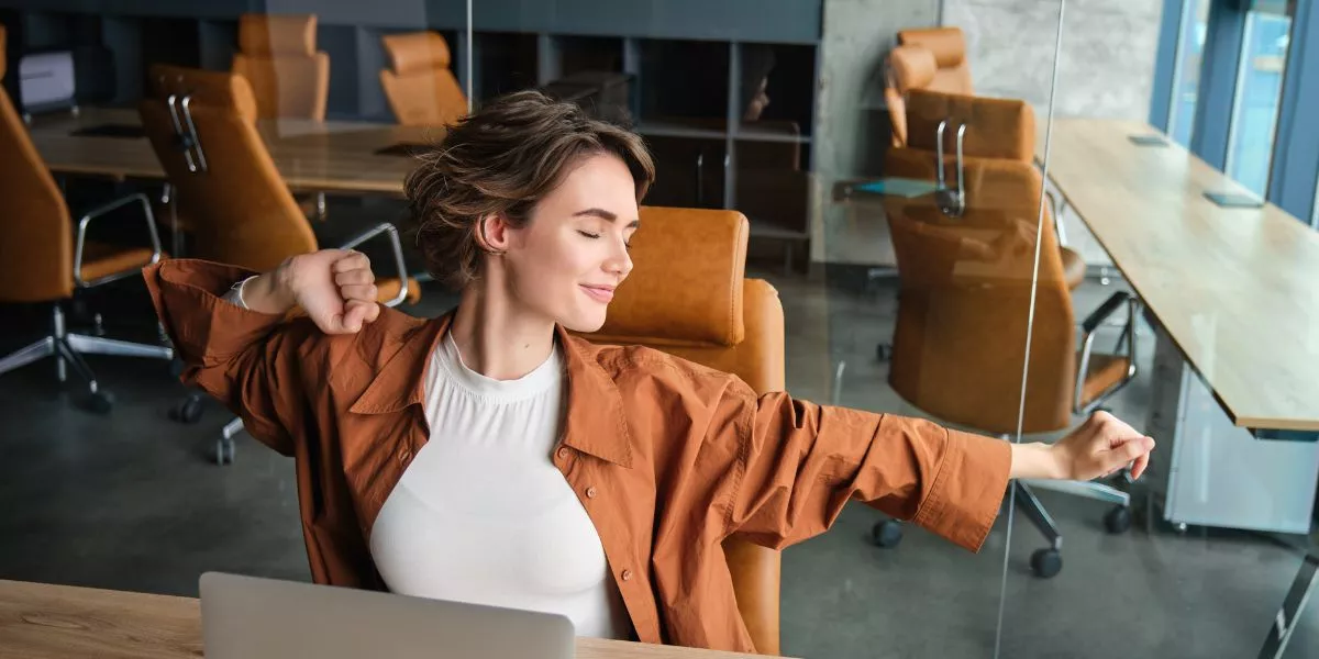 Colaboradora estirándose en una sala de reuniones moderna, representando bienestar laboral y equilibrio en el entorno de trabajo. 