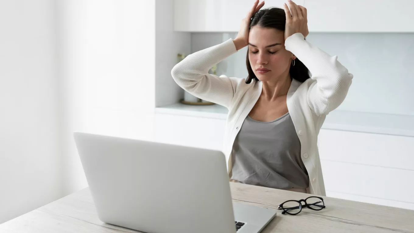 Mujer tomándose la cabeza mientras trabaja en la laptop representando el sindrome burnout 