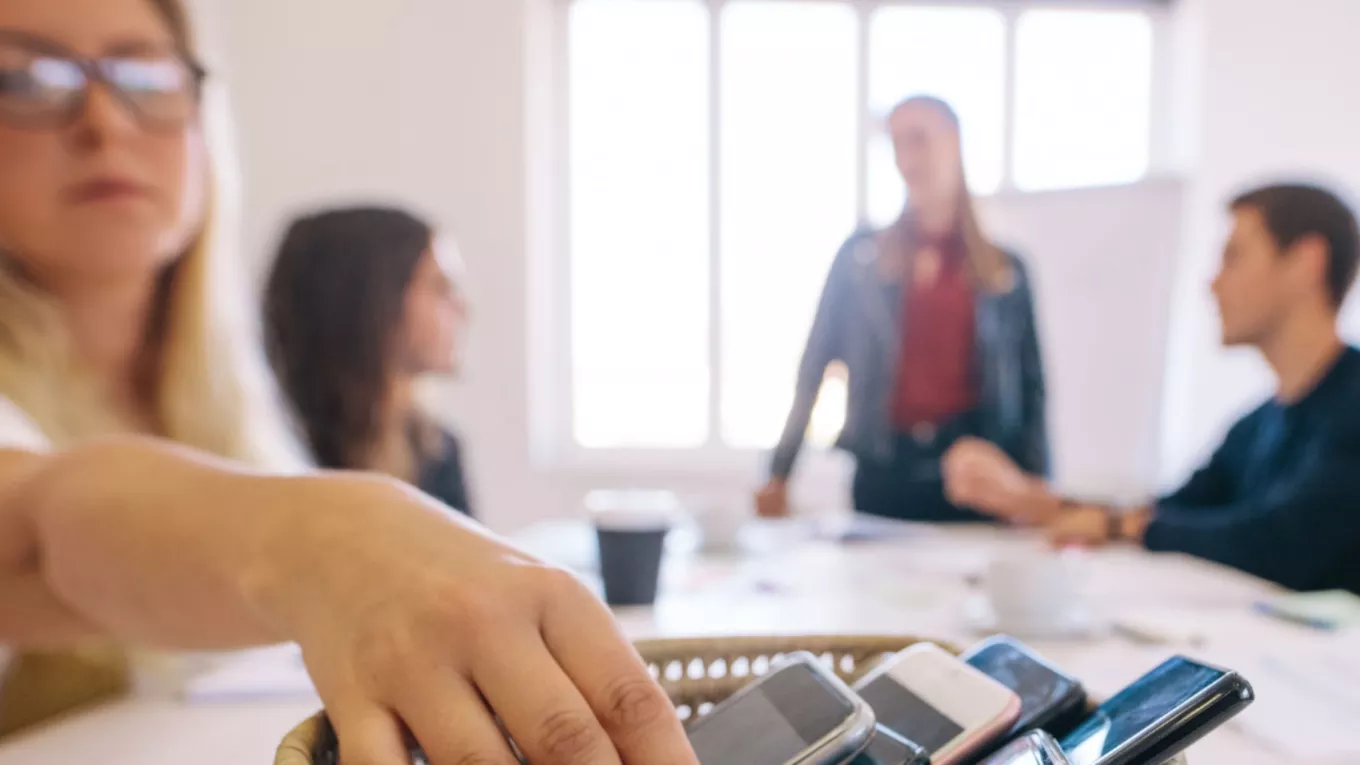 Personas dejando sus celulares en una mesa durante una reunión de trabajo para promover el bienestar digital y reducir el uso excesivo del celular. 