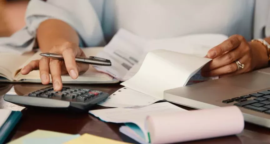 Persona revisando cuentas y documentos para consultar la devolución del IRPF en Uruguay desde una computadora portátil. 
