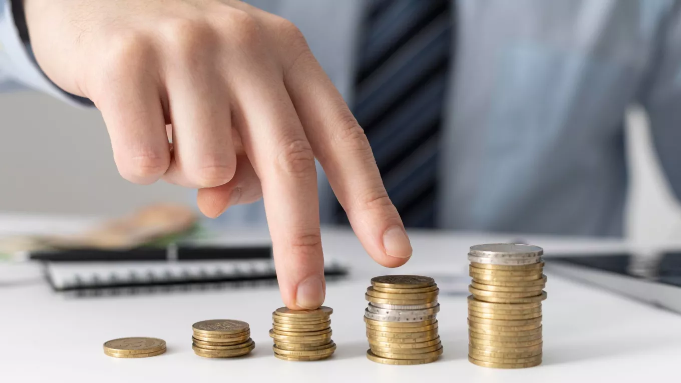 Mano acomodando pilas de monedas que representan el crecimiento de los salarios en Uruguay y la evolución del poder adquisitivo de los trabajadores. 