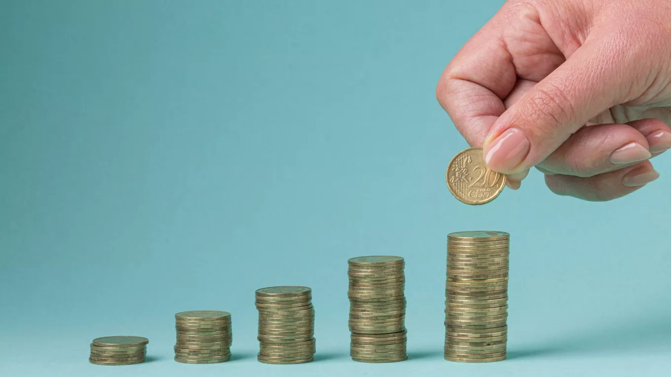 Mano colocando una moneda sobre pilas crecientes que representan el ajuste salarial 2026 en Uruguay. 
