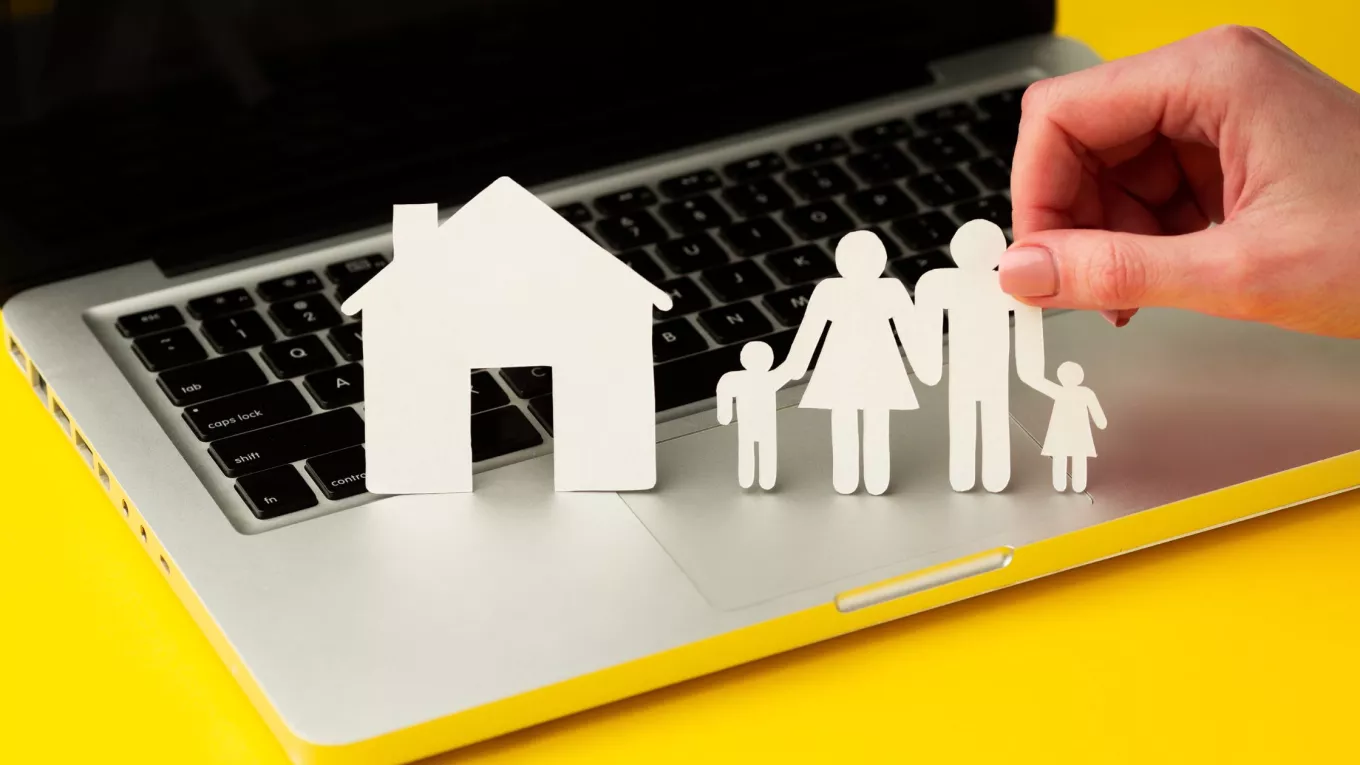 Figuras de papel de una familia y una casa sobre una computadora, como representación del equilibrio entre la vida personal y laboral. 
