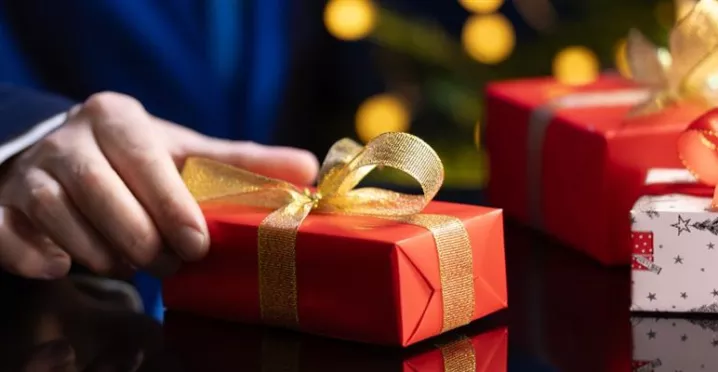 hombre sostiene un regalo de navidad en la mano con envoltorio rojo y moño dorado