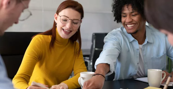 Cuatro personas en la oficina trabajando en conjunto mientras ríen y comparten un café