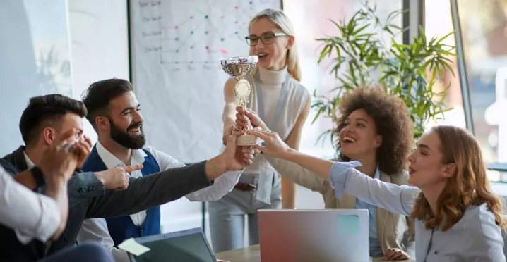 Colaboradores celebran un reconocimiento laboral levantando un trofeo en equipo durante una reunión.