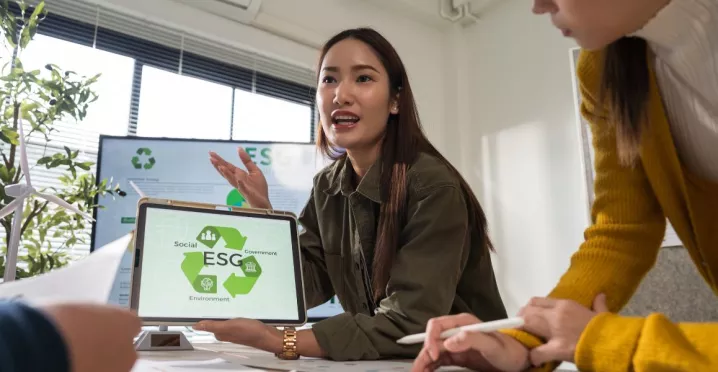 Profesional presentando una propuesta de ESG a su equipo, mostrando en una tablet los pilares de sostenibilidad ambiental, social y de gobernanza durante una reunión de trabajo.