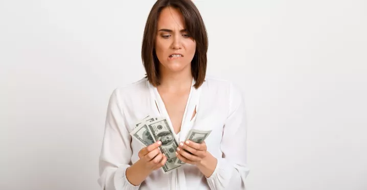 Mujer observando billetes de dinero con gesto de preocupación, reflejando la brecha entre salario real y salario percibido.