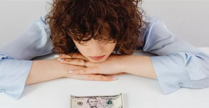 Colaboradora preocupada por su situación financiera, con un billete sobre el escritorio