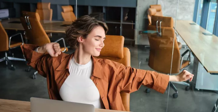 Colaboradora relajada disfrutando de sus beneficios laborales flexibles, en un entorno de trabajo moderno, enfocado en flexibilidad y bienestar