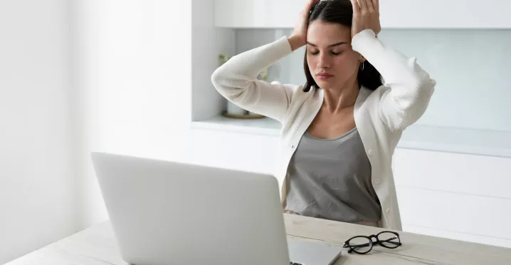 Mujer tomándose la cabeza mientras trabaja en la laptop representando el sindrome burnout