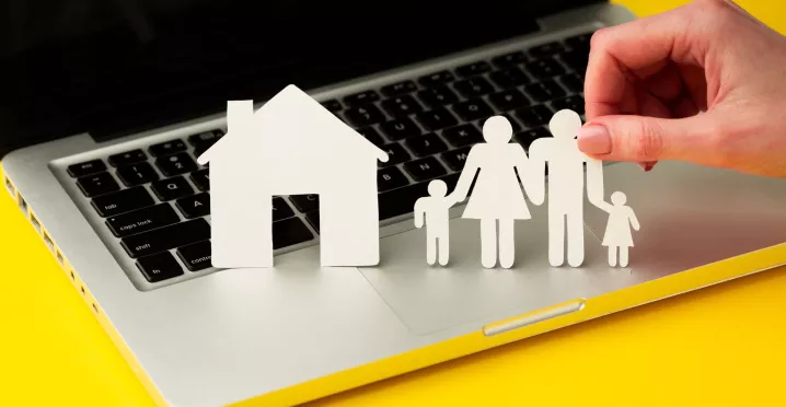 Figuras de papel de una familia y una casa sobre una computadora, como representación del equilibrio entre la vida personal y laboral.