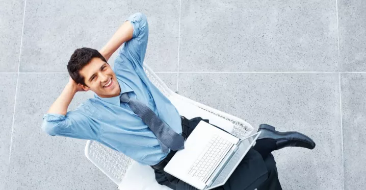 Hombre sonriente con una computadora portátil, en representación de los beneficios de la semana laboral de 4 días.