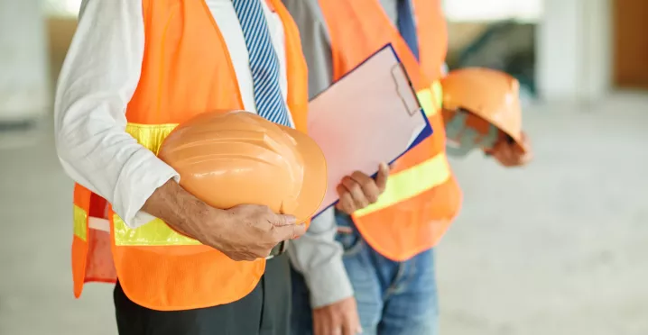 Profesionales con chalecos de seguridad sostienen cascos y una carpeta, representando la salud ocupacional en el trabajo.