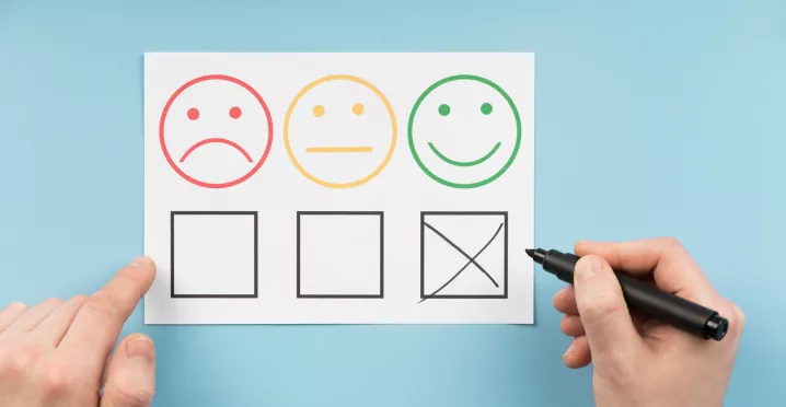 Persona marca la opción positiva en una encuesta de satisfacción laboral con caras que representan distintos niveles de conformidad.