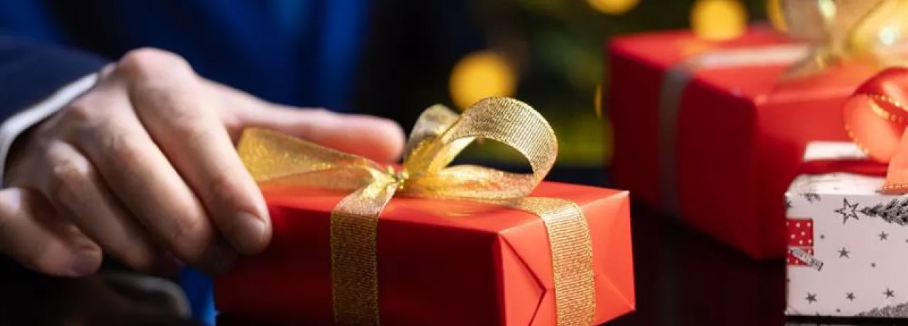 hombre sostiene un regalo de navidad en la mano con envoltorio rojo y moño dorado