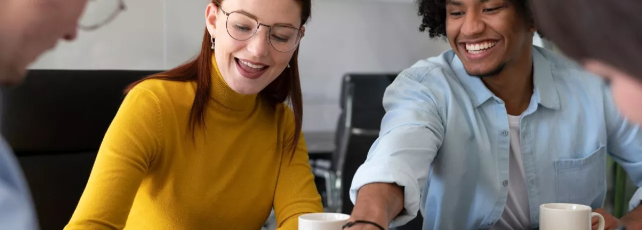 Cuatro personas en la oficina trabajando en conjunto mientras ríen y comparten un café