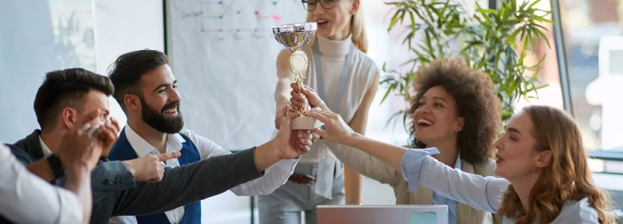 Colaboradores celebran un reconocimiento laboral levantando un trofeo en equipo durante una reunión.