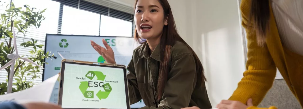 Profesional presentando una propuesta de ESG a su equipo, mostrando en una tablet los pilares de sostenibilidad ambiental, social y de gobernanza durante una reunión de trabajo.