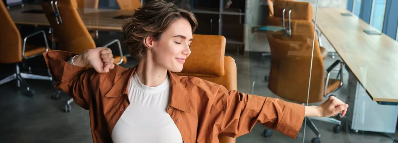 Colaboradora estirándose en una sala de reuniones moderna, representando bienestar laboral y equilibrio en el entorno de trabajo.