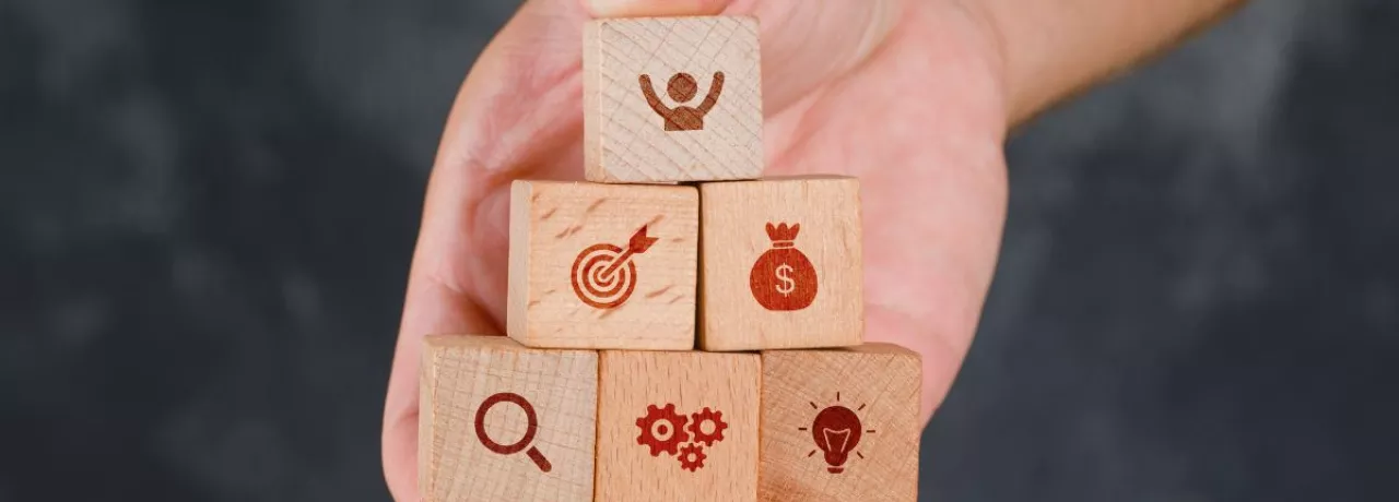 Mano sosteniendo bloques de madera en forma de pirámide con íconos que representan beneficios para empresas y programa de beneficios para empleados.