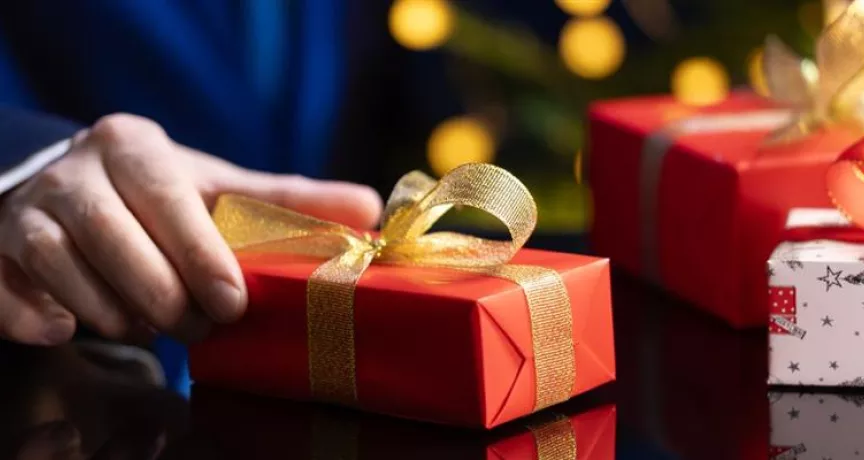 hombre sostiene un regalo de navidad en la mano con envoltorio rojo y moño dorado