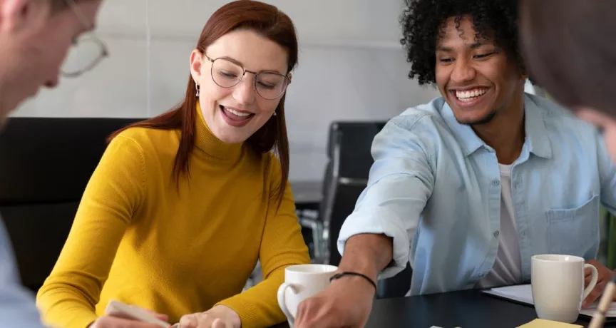 Cuatro personas en la oficina trabajando en conjunto mientras ríen y comparten un café