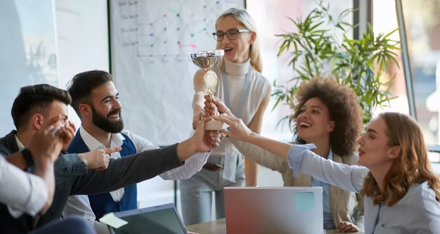 Colaboradores celebran un reconocimiento laboral levantando un trofeo en equipo durante una reunión.