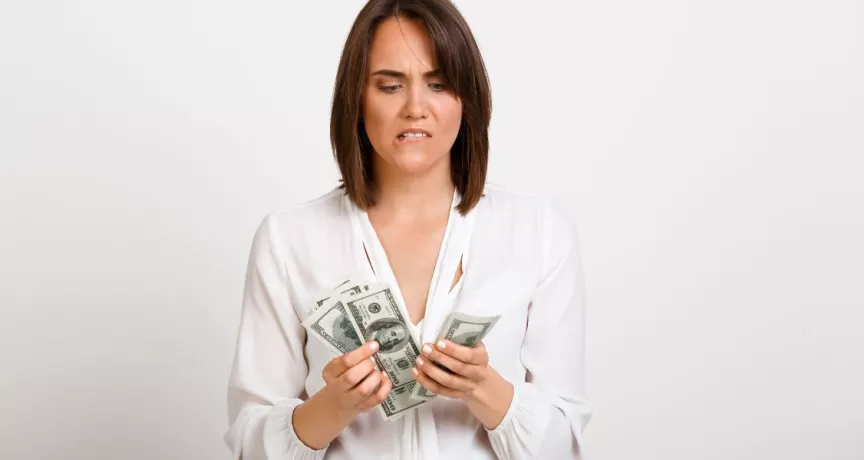 Mujer observando billetes de dinero con gesto de preocupación, reflejando la brecha entre salario real y salario percibido.