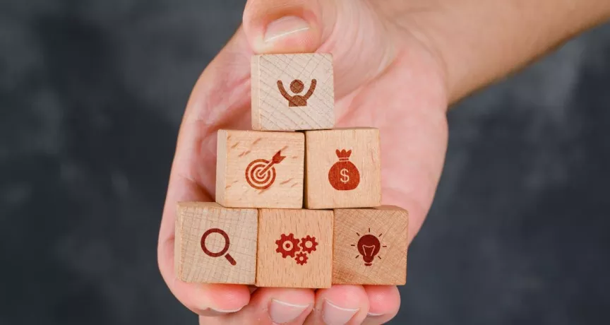 Mano sosteniendo bloques de madera en forma de pirámide con íconos que representan beneficios para empresas y programa de beneficios para empleados.