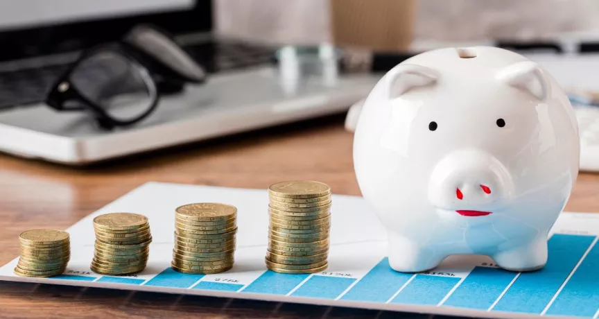 Alcancía con monedas sobre gráfico financiero y laptop de fondo representando el ROI en beneficios corporativos y ahorro fiscal en Uruguay