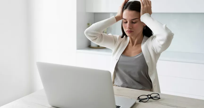 Mujer tomándose la cabeza mientras trabaja en la laptop representando el sindrome burnout
