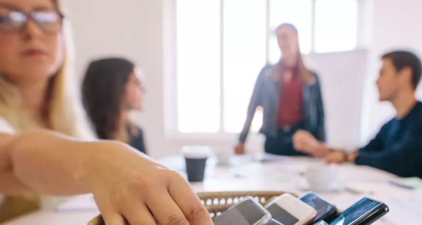 Personas dejando sus celulares en una mesa durante una reunión de trabajo para promover el bienestar digital y reducir el uso excesivo del celular.