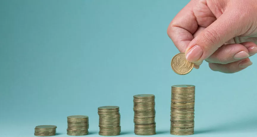Mano colocando una moneda sobre pilas crecientes que representan el ajuste salarial 2026 en Uruguay.