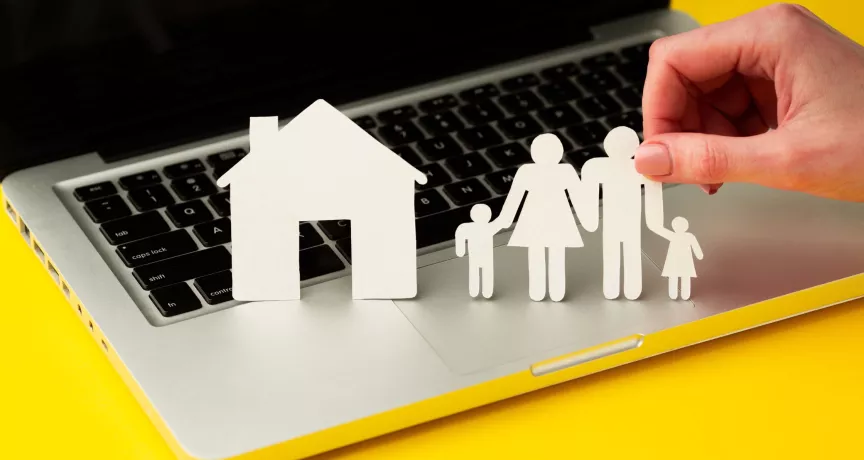 Figuras de papel de una familia y una casa sobre una computadora, como representación del equilibrio entre la vida personal y laboral.