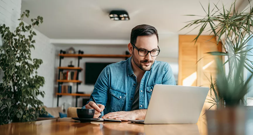 Hombre trabajando con una computadora portátil y tomando notas para planificar una estrategia de beneficios laborales en Uruguay.