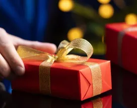hombre sostiene un regalo de navidad en la mano con envoltorio rojo y moño dorado