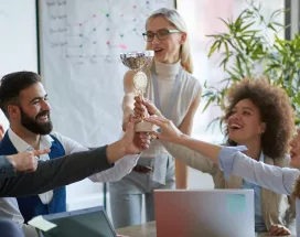 Colaboradores celebran un reconocimiento laboral levantando un trofeo en equipo durante una reunión.