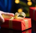 hombre sostiene un regalo de navidad en la mano con envoltorio rojo y moño dorado