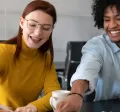 Cuatro personas en la oficina trabajando en conjunto mientras ríen y comparten un café