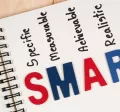 Cuaderno con la palabra SMART y sus componentes específicos, medibles, alcanzables, relevantes y con plazo, representando la metodología para definir objetivos SMART.
