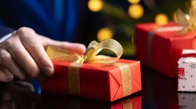 hombre sostiene un regalo de navidad en la mano con envoltorio rojo y moño dorado