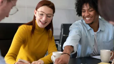 Cuatro personas en la oficina trabajando en conjunto mientras ríen y comparten un café