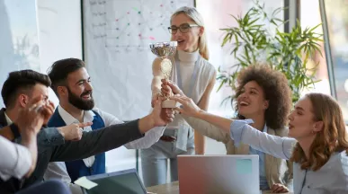 Colaboradores celebran un reconocimiento laboral levantando un trofeo en equipo durante una reunión.
