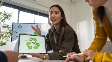 Profesional presentando una propuesta de ESG a su equipo, mostrando en una tablet los pilares de sostenibilidad ambiental, social y de gobernanza durante una reunión de trabajo.