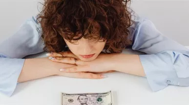 Colaboradora preocupada por su situación financiera, con un billete sobre el escritorio